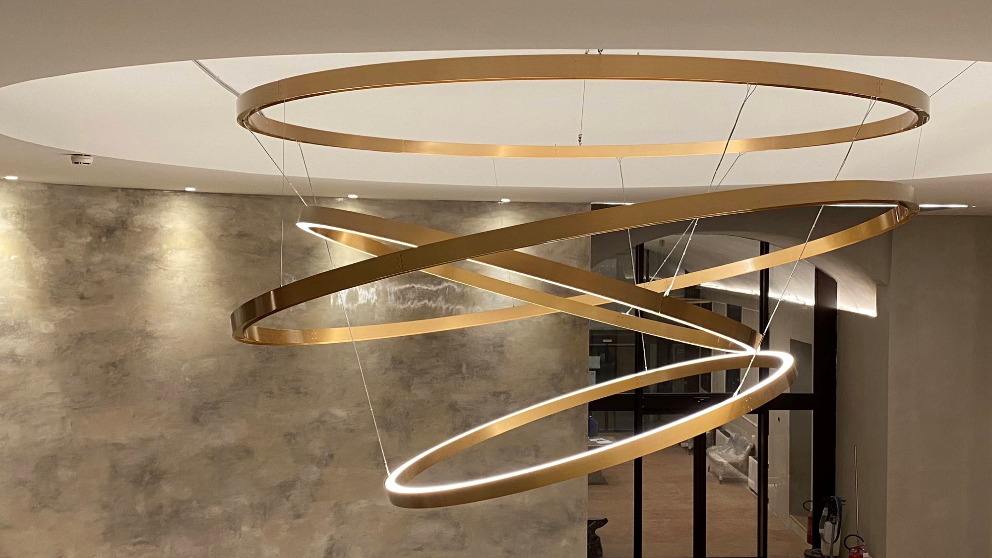 É um candeeiro de dimensões generosas, composto por quatro anéis de latão, dois dos quais luminosos com luz direta e indireta.